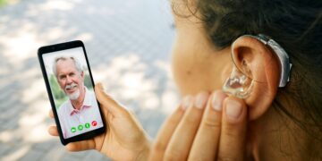 Adult woman with a hearing aid in her ear communicates with her father via video communication via a smartphone. Full human life with hearing aids