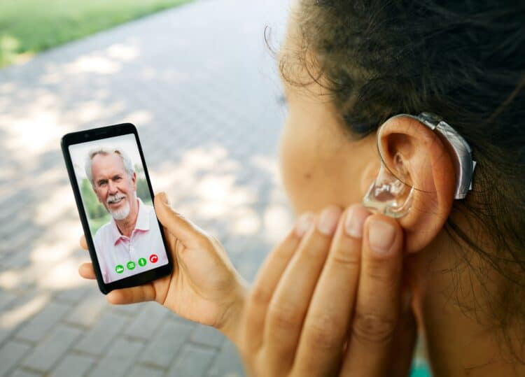 Adult woman with a hearing aid in her ear communicates with her father via video communication via a smartphone. Full human life with hearing aids