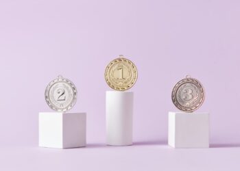Photo by DS stories: https://www.pexels.com/photo/medals-on-pedestal-on-pink-studio-background-7267588/