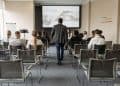 Photo by Pavel Danilyuk from Pexels: https://www.pexels.com/photo/a-man-walking-on-aisle-between-chairs-with-people-sitting-8761317/